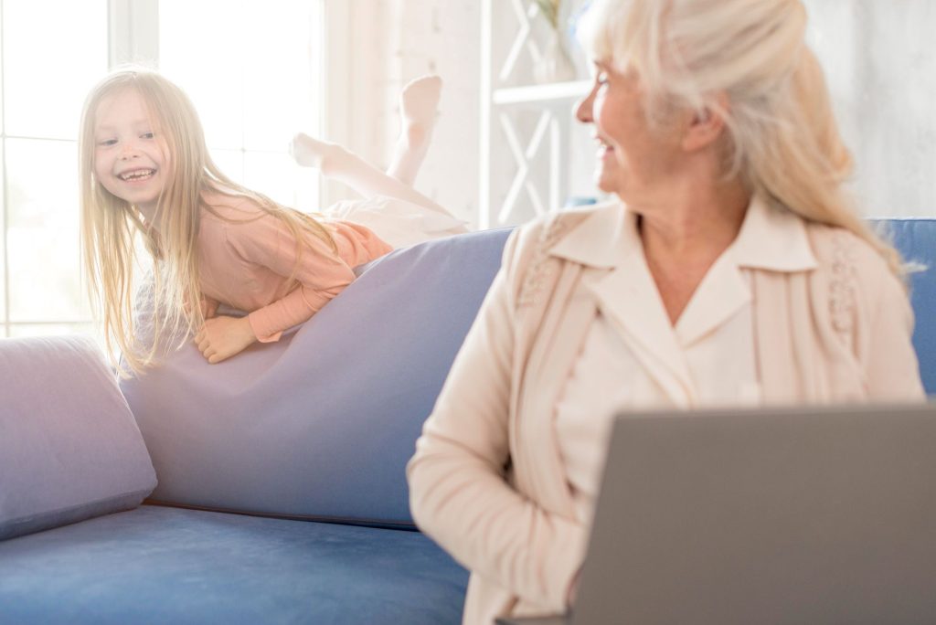 Older adult smiling at home during a virtual psychiatry session while spending time with her granddaughter.